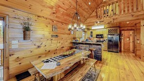 Ein Holzblockbau-Innenraum mit Esstisch, Küchenzeile und einer großen Chandelier.
