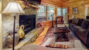 A cozy cabin interior with a stone fireplace, wooden walls, a comfortable sofa, and a television. - Indian Rock Lake Cabin (Cherry Log)