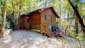 A wooden cabin with a staircase leading to a deck, surrounded by trees. - Indian Rock Lake Cabin (Cherry Log)
