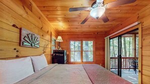 A wooden cabin bedroom with a bed, a ceiling fan, a dresser, and a view of the outdoors through a sliding door. - Indian Rock Lake Cabin (Cherry Log)