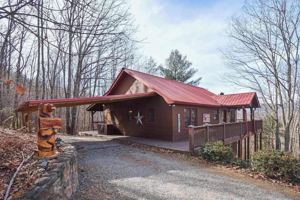 A rustic cabin with a red roof, a wooden deck, and a stone wall.