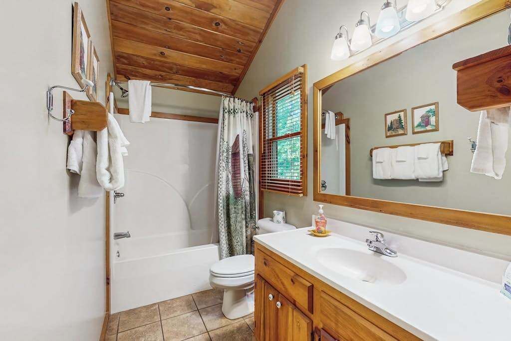 Ein Badezimmer mit Holzboden, einer Badewanne, einer Toilette, einem Waschbecken mit Spiegel und einer Duschvorhang.