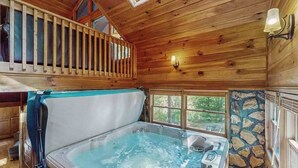 L’intérieur d’un chalet en bois comprend un bain à remous, un plafond en bois, un mur en pierre et un balcon.