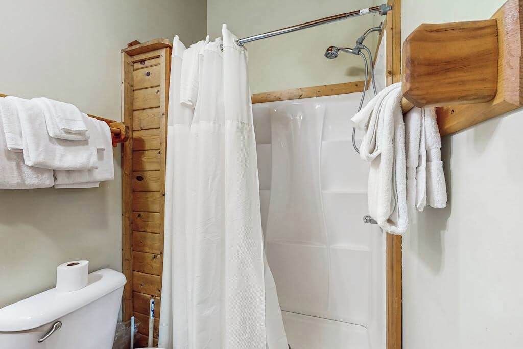 A bathroom with a shower, toilet, and wooden paneling.