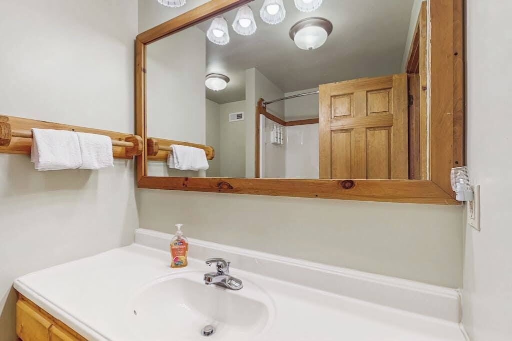 Un baño con un espejo grande, un lavabo blanco y una puerta de madera.