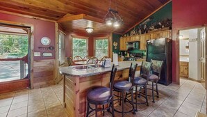 Une cuisine avec des meubles de rangement en bois, un îlot central doté de tabourets, un réfrigérateur et une horloge au mur.