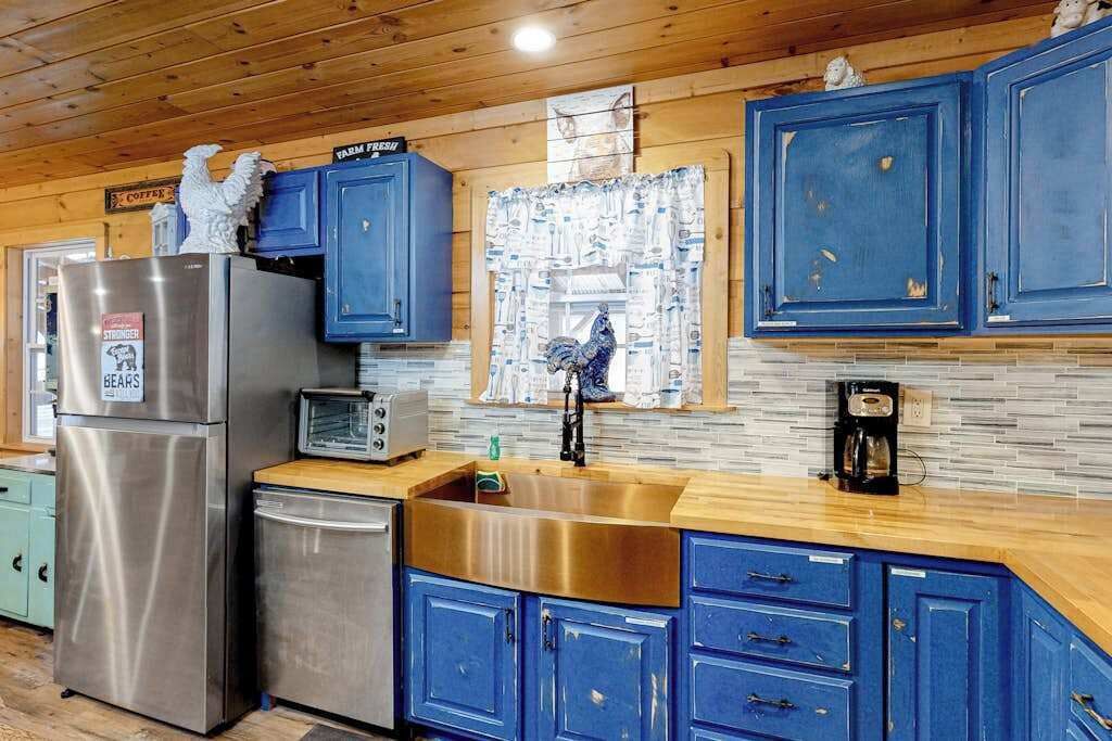 A kitchen with blue cabinets, stainless steel appliances, and a tiled backsplash.