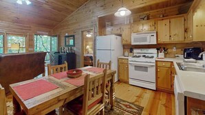 Ein Holzblockbau-Innenraum mit Esstisch, Stühlen, Kühlschrank, Mikrowelle und Herd.
