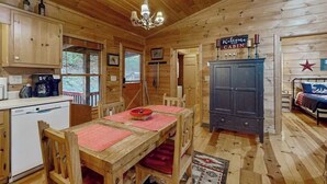 Ein Blockhaus-Interieur mit Holzwänden, einem Esstisch mit roten Untersetzern, einem dunklen Schrank und einem Bett mit Sterndekoration.