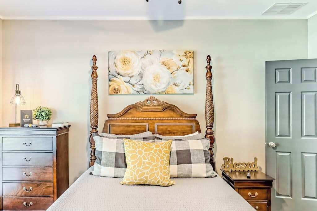 Quarto com cama de dossel, mesa de cabeceira com abajur, cômoda e porta.