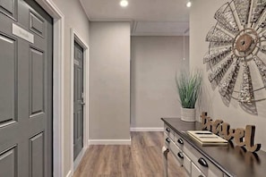 A hallway with grey doors, a wooden floor, a decorative wall piece, a potted plant, and a wooden bench with the word 'travel' on it.