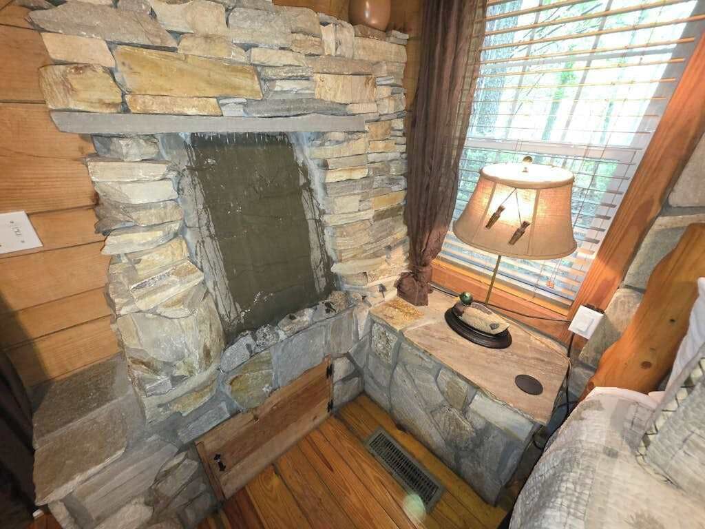 A stone fireplace with a bench, a lamp, and a window with blinds.