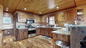 A wooden cabin-style kitchen with wooden cabinets, a stainless steel oven, and a granite countertop. - Bougie Bear Cabin Stay (Morganton)