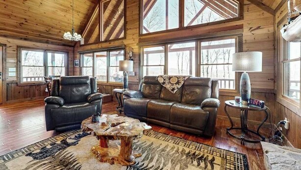 A wooden cabin interior with two leather sofas, a coffee table, and large windows. - Bougie Bear Cabin Stay (Morganton)