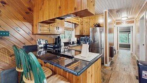 Interior de una cabaña de madera con isla de cocina, sillas y refrigerador.