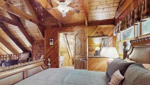 Un dormitorio de cabaña de madera con una cama, un ventilador de techo y vistas al exterior.