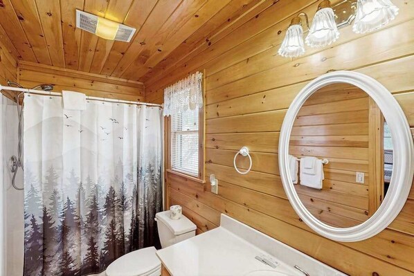 A wooden cabin bathroom with a shower curtain, toilet, sink, and a round mirror. - Wolf Creek Retreat Lodge (Mineral Bluff)