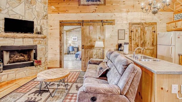 A log cabin interior with a stone fireplace, a sofa, a kitchen area, and a bear decoration on the wall. - Amazing Grace - Mountain Retreat (Blue Ridge)