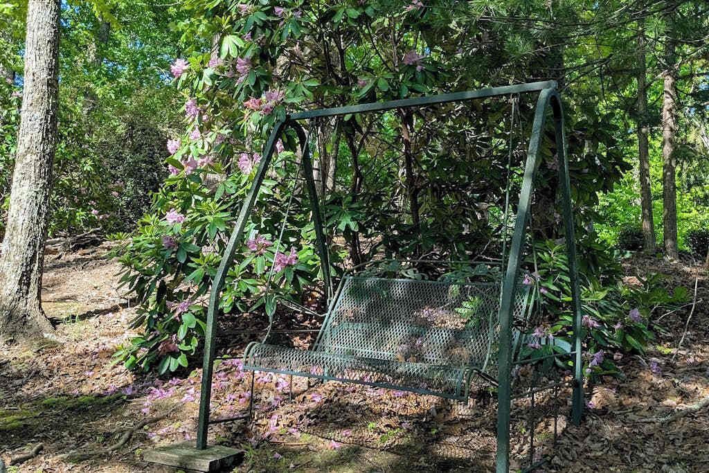 Une chaise à bascule en métal, installée dans un espace boisé.