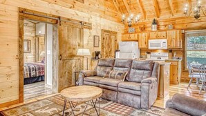 A wooden cabin interior with a sofa, a dining table, a kitchen area, and a view of the outdoors. - Amazing Grace - Mountain Retreat (Blue Ridge)
