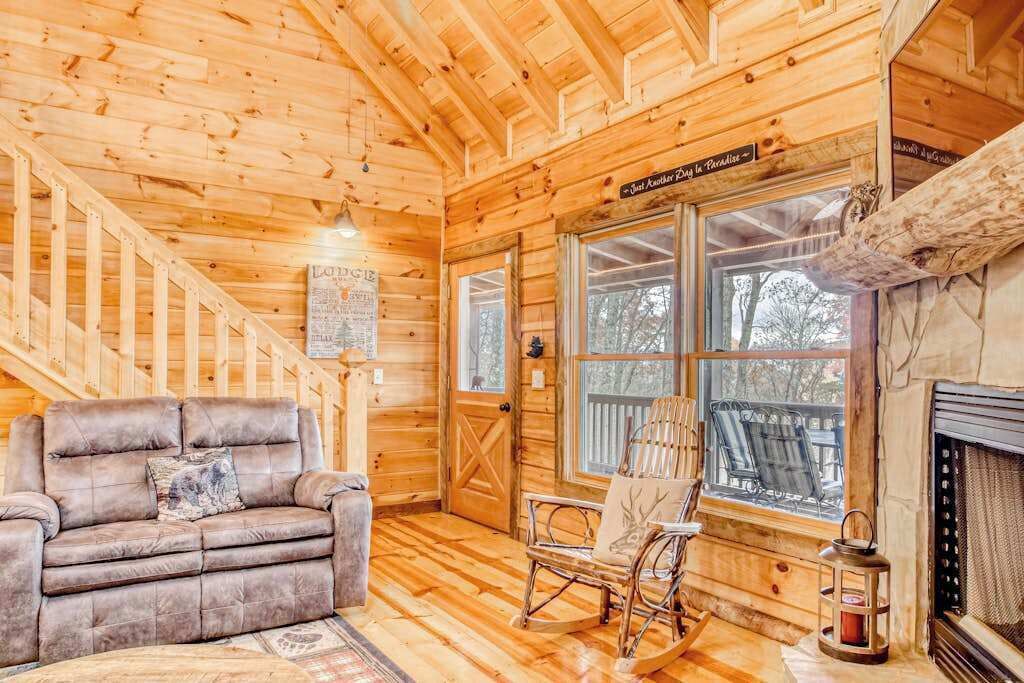 A wooden cabin interior with a sofa, rocking chair, and fireplace.