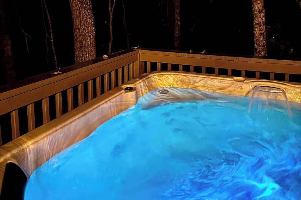 A hot tub with a wooden deck and a dark background.