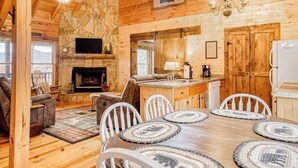 A log cabin interior with a stone fireplace, wooden dining table, and a kitchen area. - Amazing Grace - Mountain Retreat (Blue Ridge)