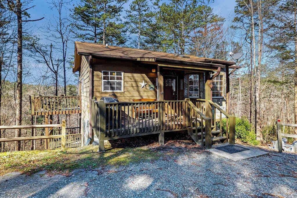 A wooden cabin with a porch, surrounded by trees.