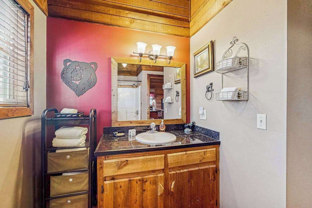 Une salle de bain avec un meuble-lavabo en bois, un miroir avec éclairage intégré, un porte-serviettes et une étagère fixée au mur.
