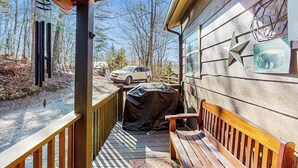 En træterrasse med en bænk, et overdækket grillområde, og en bil parkeret ude foran.