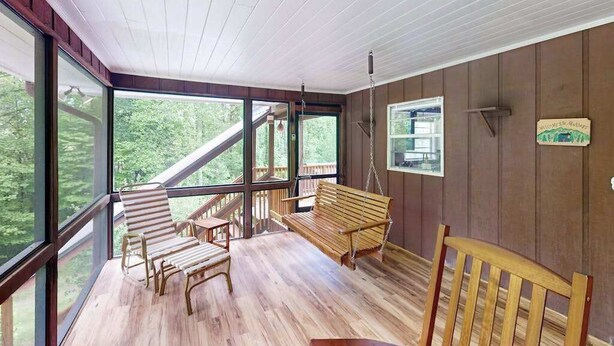 En träveranda med en hänggunga, en bänk och en stol.