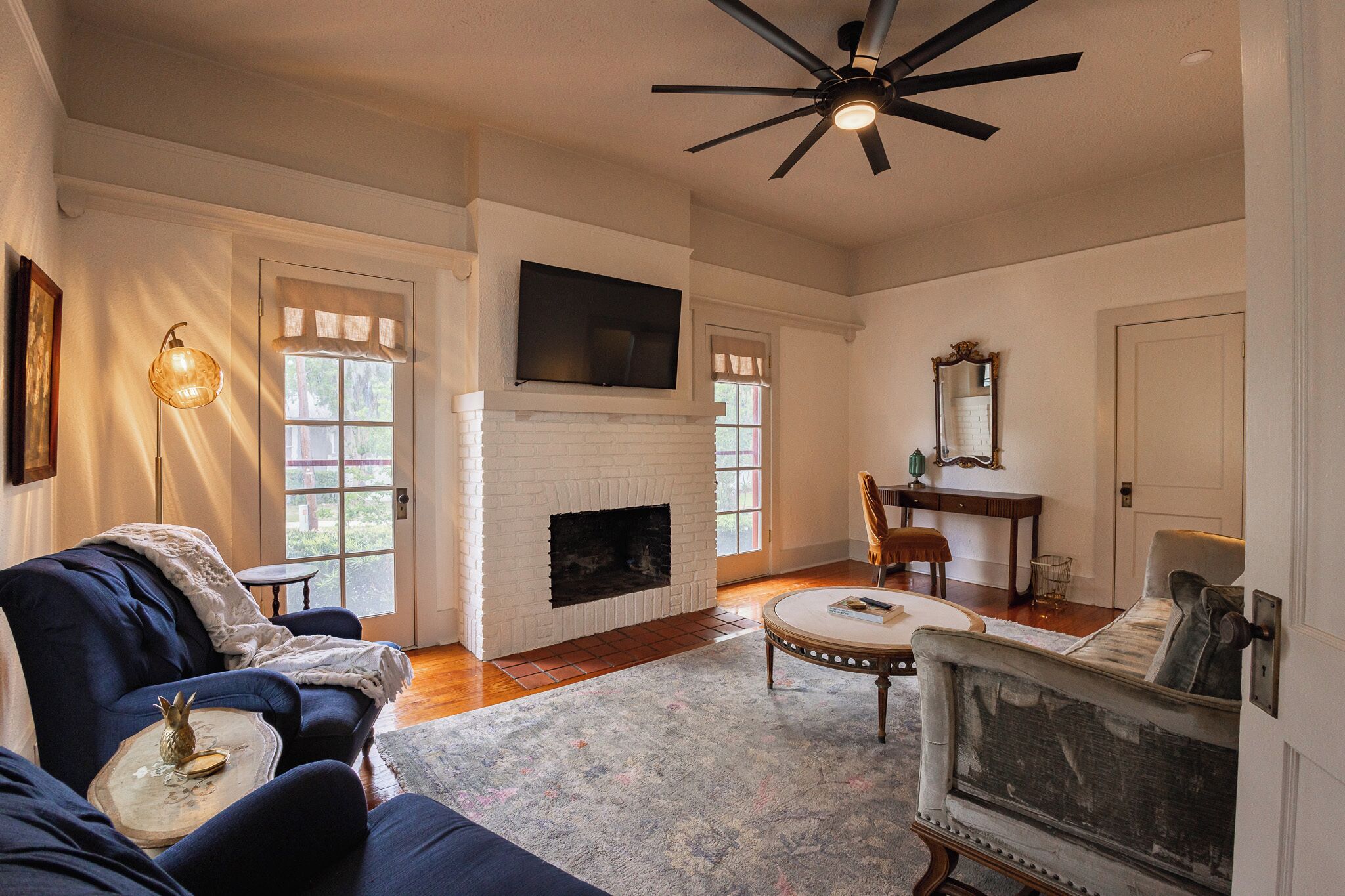 A living room with a fireplace, a ceiling fan, and a television mounted above it.