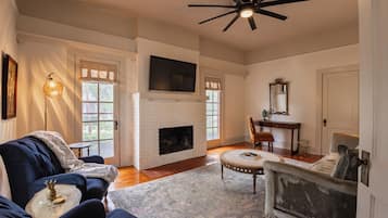 A living room with a fireplace, a ceiling fan, and a television mounted above it.