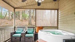 Un espace extérieur abrité, aménagé avec des meubles en osier, un jacuzzi et offrant une vue sur la forêt.