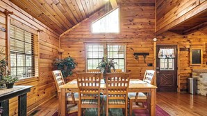 L’intérieur d’un chalet en bois, avec une table à manger, des chaises et une cheminée.