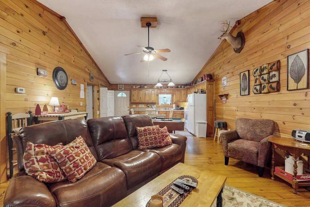 Ein gemütliches Wohnzimmer mit einer Ledersofa, einem gemusterten Sessel, einem Holztisch und einem Deckenventilator.
