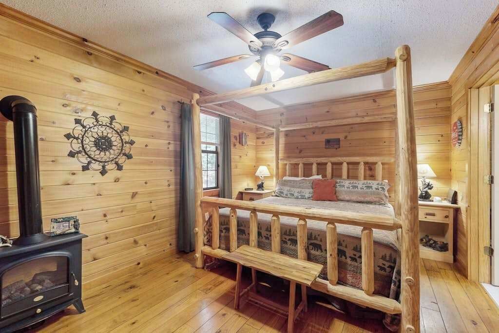 A log cabin bedroom with a bed, a ceiling fan, a fireplace, and a window.