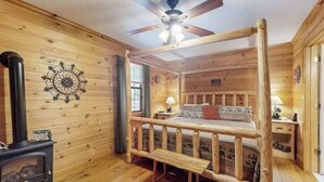 A log cabin bedroom with a bed, a ceiling fan, a fireplace, and a window. - Lazy Acres Cabin Sautee (Sautee Nacoochee)