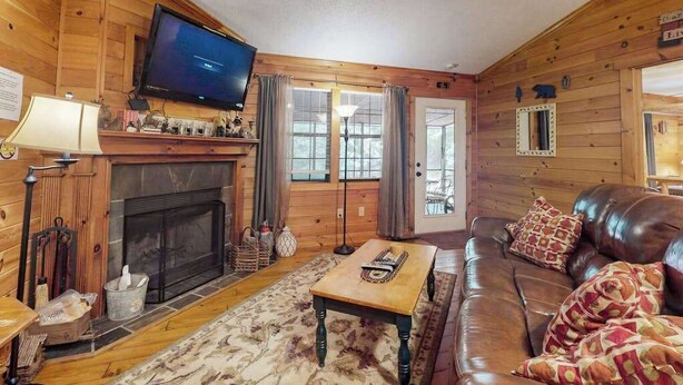 A log cabin interior with a fireplace, leather sofa, television, and wooden walls. - Lazy Acres Cabin Sautee (Sautee Nacoochee)