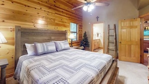 A wooden cabin bedroom with a bed, a ceiling fan, a Christmas tree, and a door. - Bear Necessity Cabin (Hiawassee)