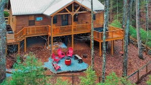 A wooden cabin with a deck, a fire pit, and red chairs. - Bear Necessity Cabin (Hiawassee)