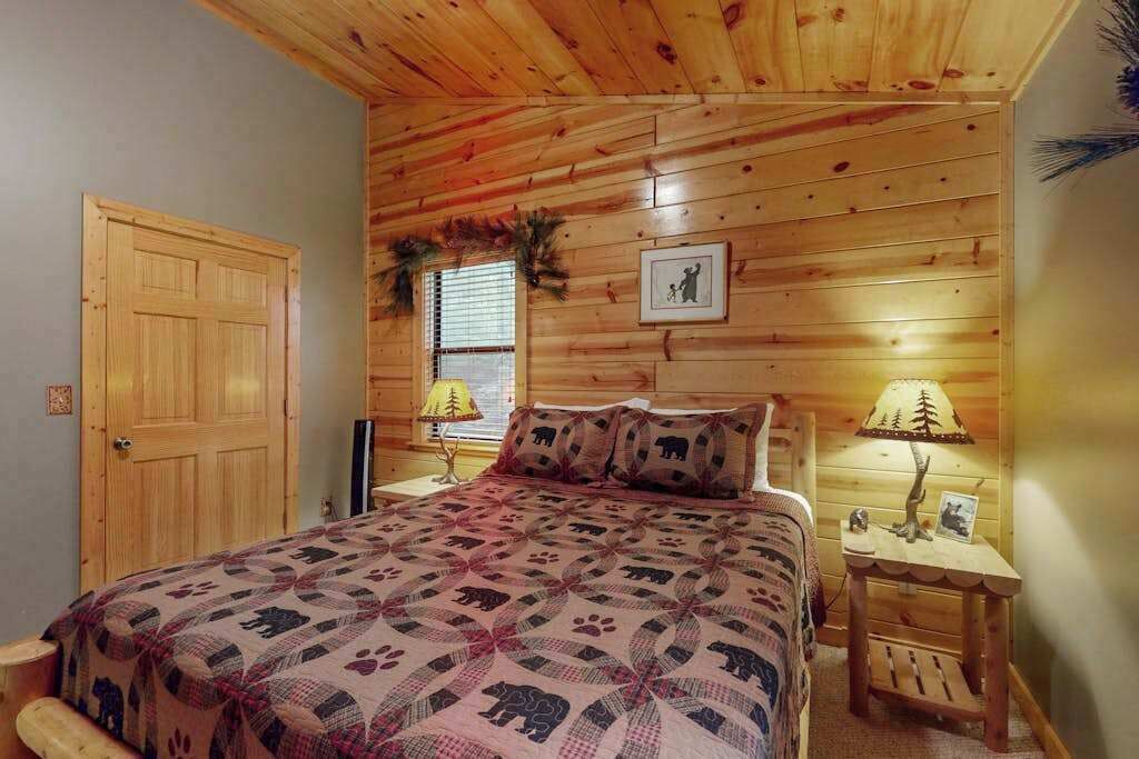 Una habitación con paneles de madera, una cama con colcha estampada, un ventanal con persianas y una mesita de noche con lámpara.
