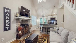 Ein Wohnzimmer mit Kamin, Fernseher, einer Couch und einer Küche im Hintergrund.