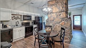 Une cuisine avec des meubles blancs, un mur d’accent en pierre, un lustre et un coin repas comprenant une table et des chaises.