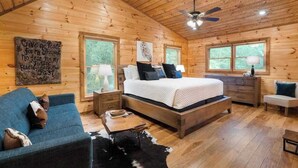 Interior de una cabaña de madera con cama, sofá y ventilador de techo.