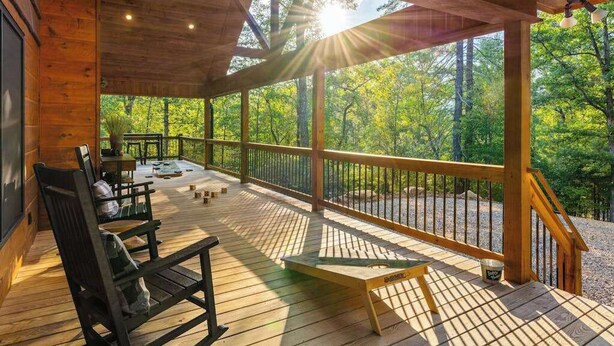 Una terraza de madera con mobiliario exterior, una mesa y vistas a un bosque.