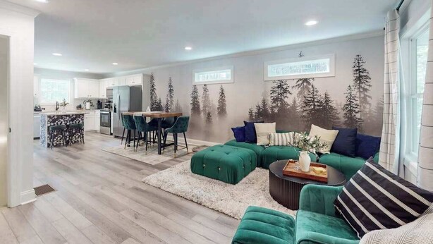 Una sala de estar moderna con un sofá verde, una zona de comedor y una cocina al fondo.