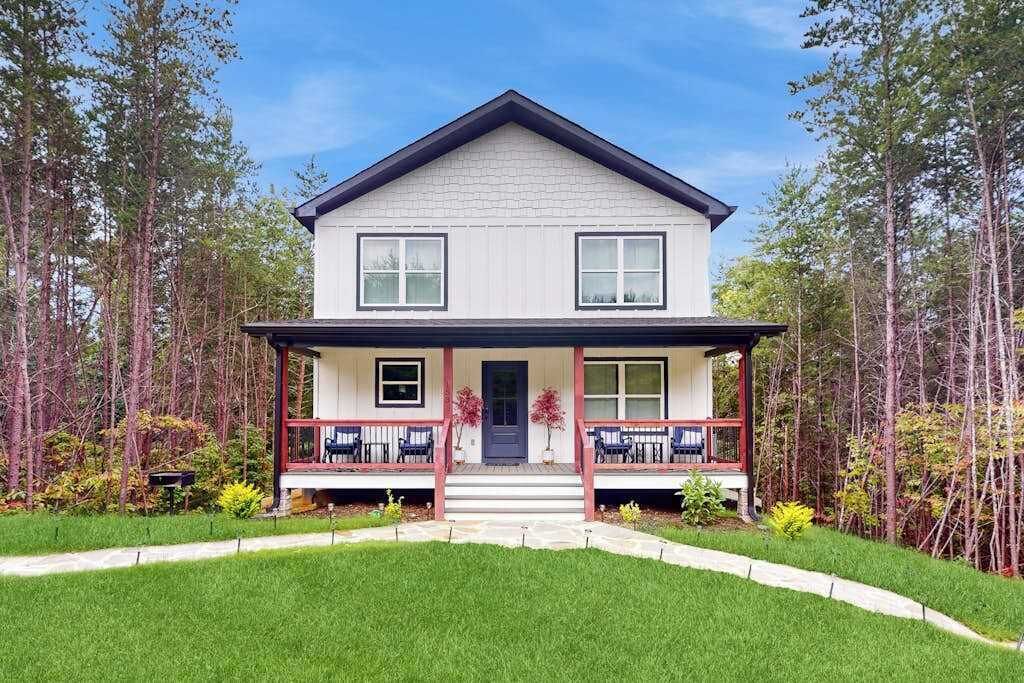 Une maison à deux étages avec un porche à l’avant, une porte centrale et un petit jardin devant.