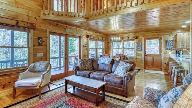 A spacious wooden cabin with a loft bedroom, a living room with a leather sofa, and a dining area. - Dogwood Overlook Cabin (Mineral Bluff)