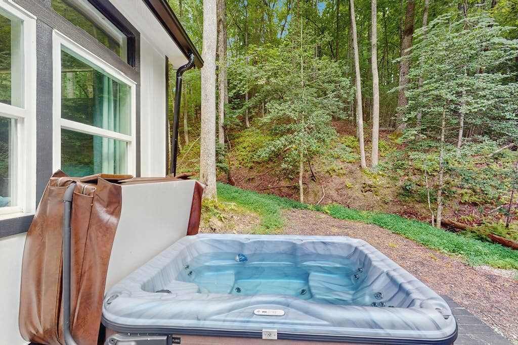 Un bain à remous situé à l’extérieur d’une maison, avec une zone boisée en arrière-plan.